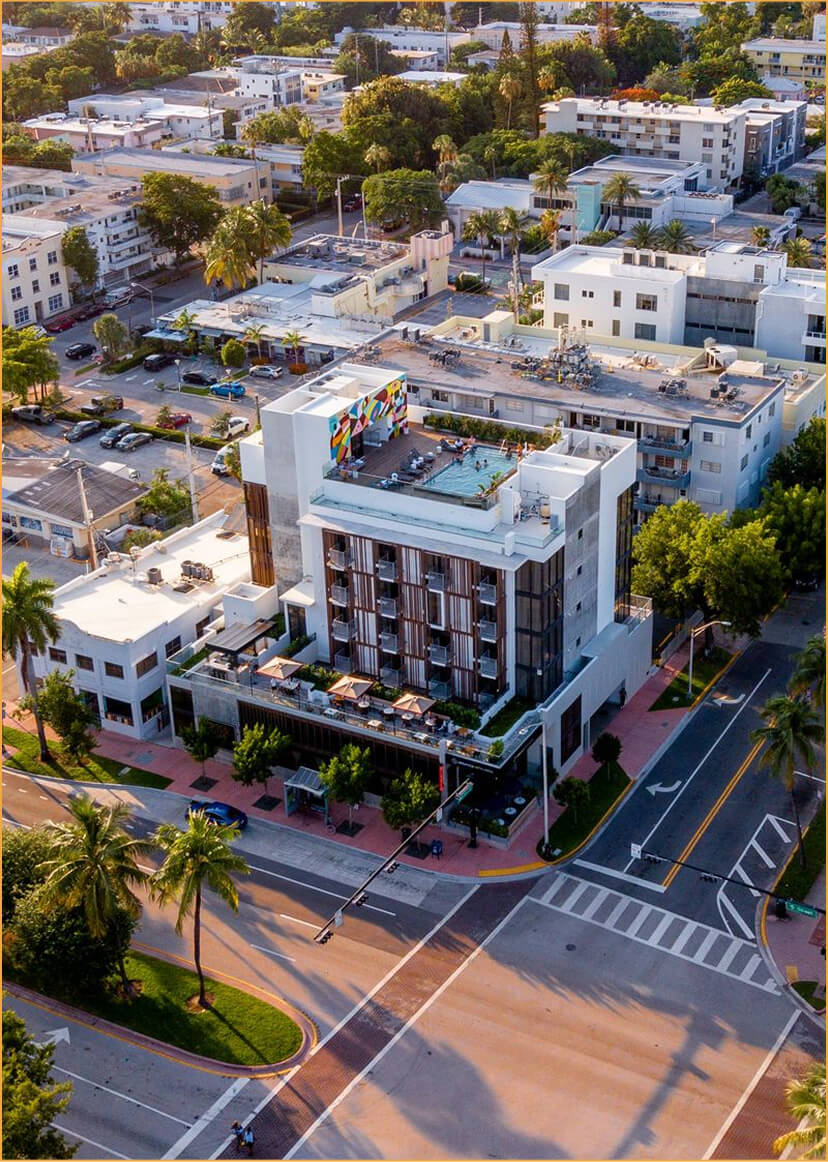 Aerial view of a modern multistory hotel with a rooftop pool and terrace.