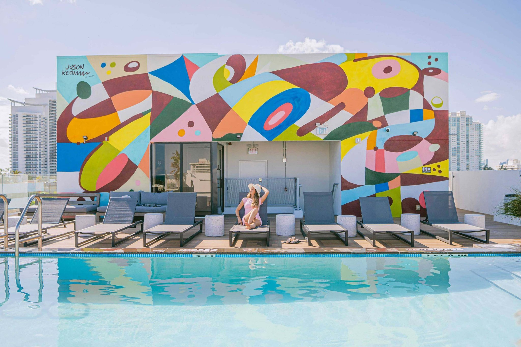 A colorful mural on the side of a building next to a pool with lounge chairs.