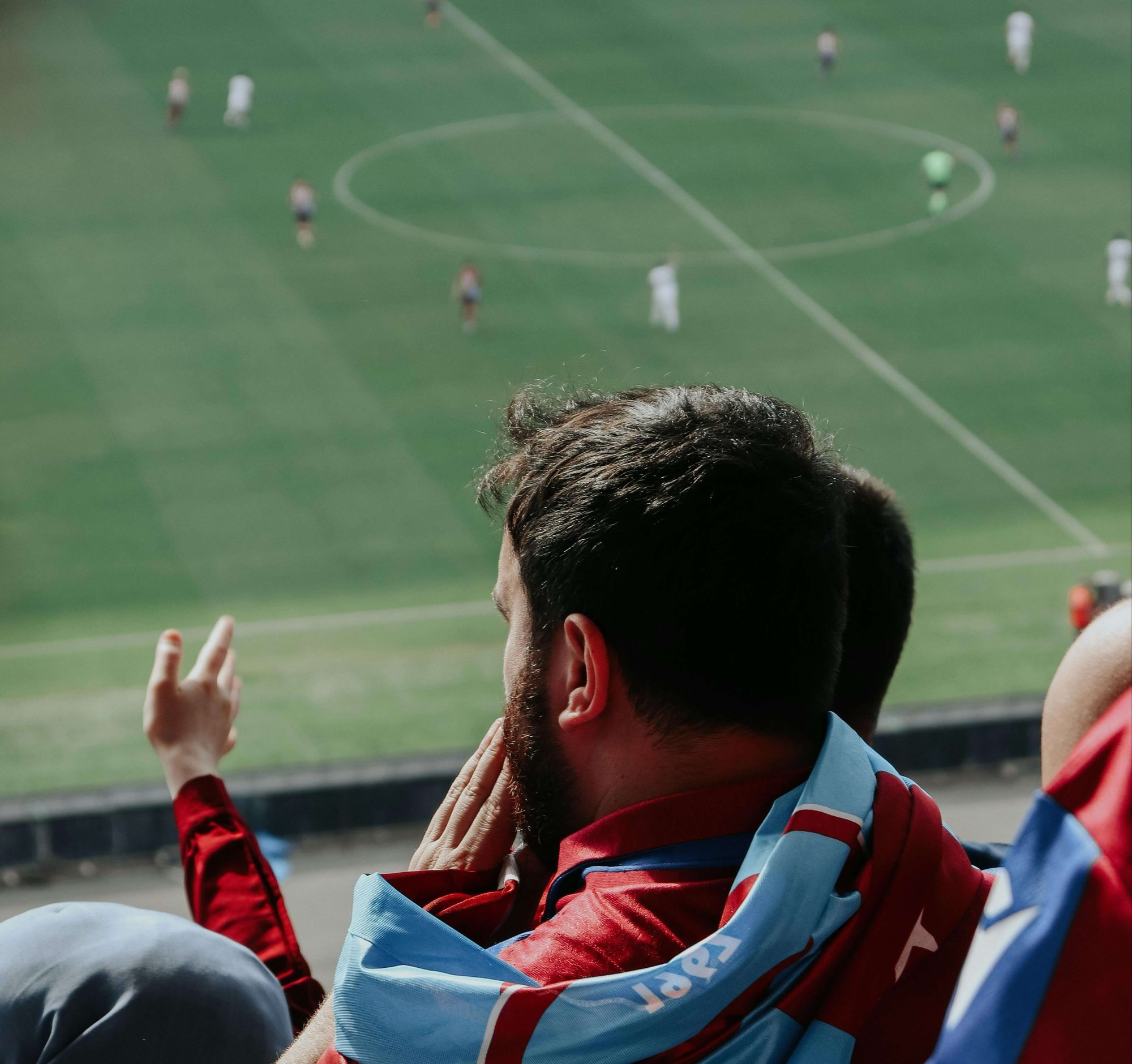 Football fan in maroon and sky-blue jersey watching a match from the stadium stands