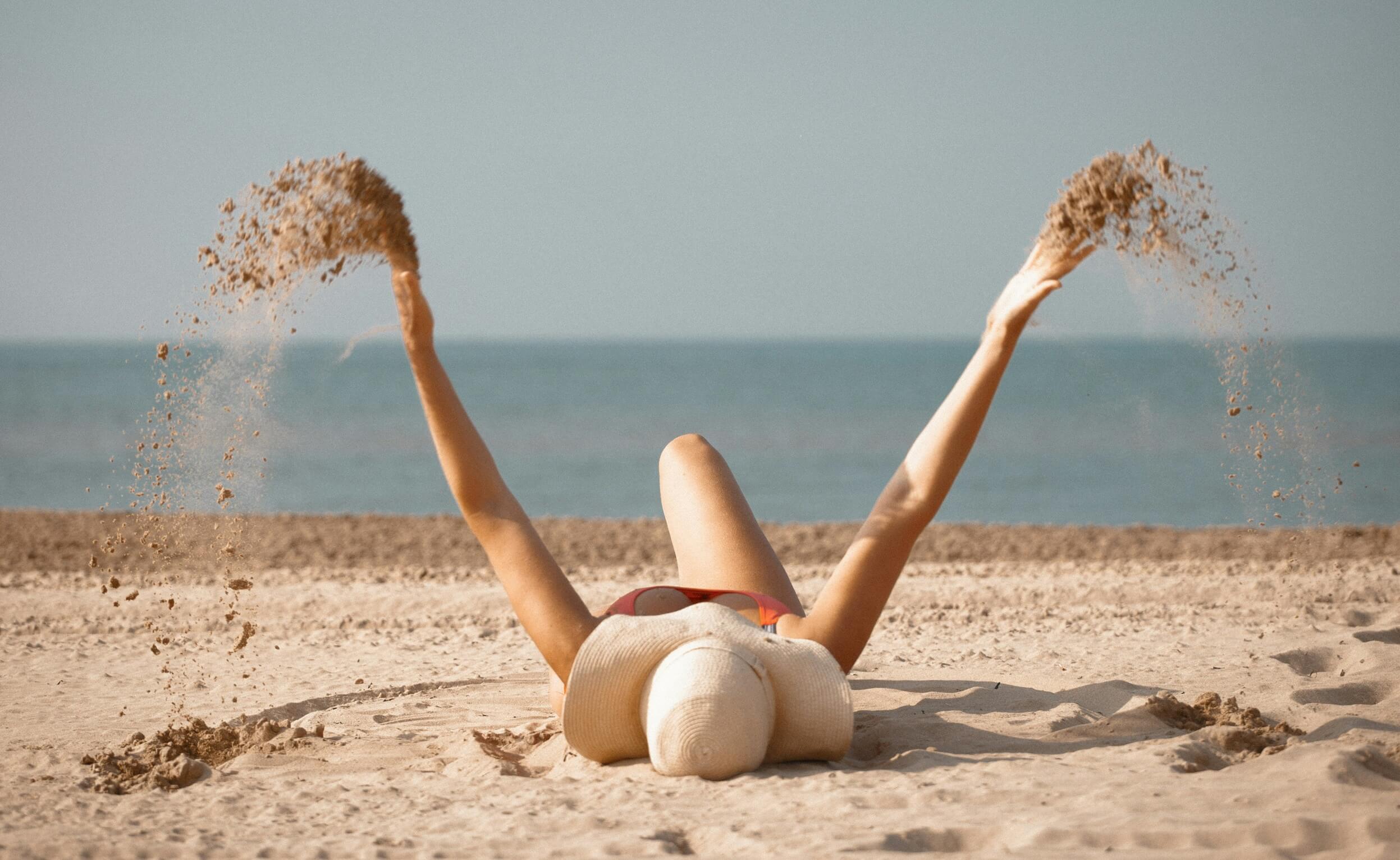 A woman laying on sand with her arms in the air