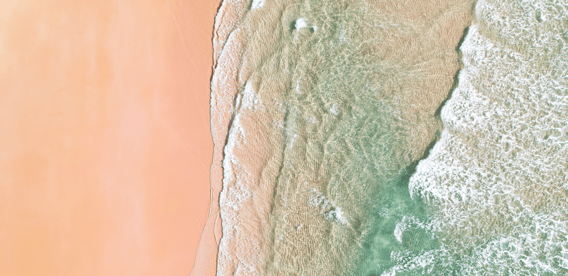Aerial beach view with clear turquoise water, white wave foam, and golden sand coastline
