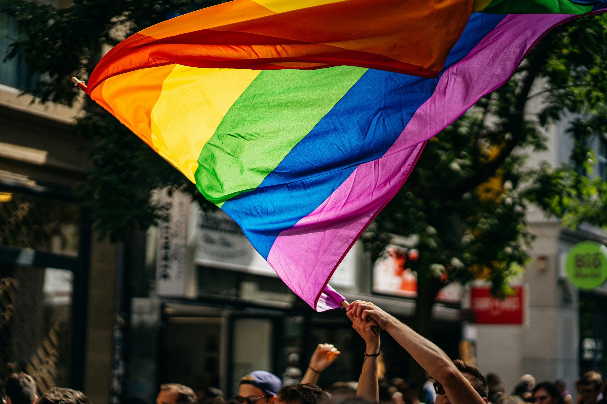 A LGBTQ+ flag being swung in a parade. 