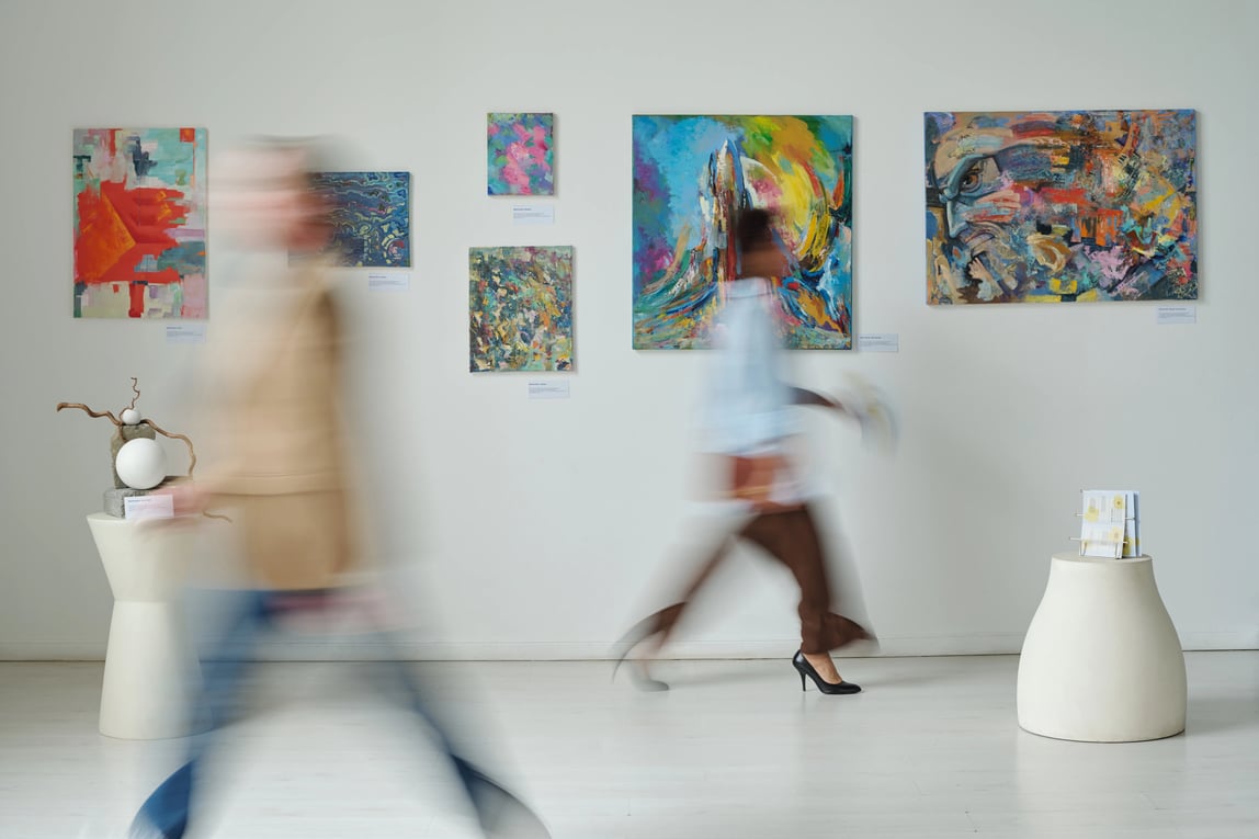 People walking past paintings displayed in a modern art gallery